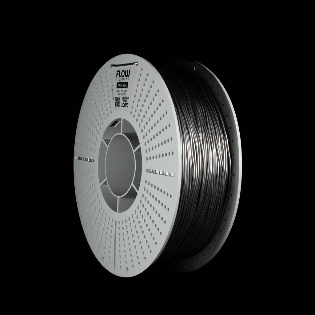 A spool of metallic space grey 3D printing filament on a solid black background, with the brand name FLOW visible on the top of the perforated spool.