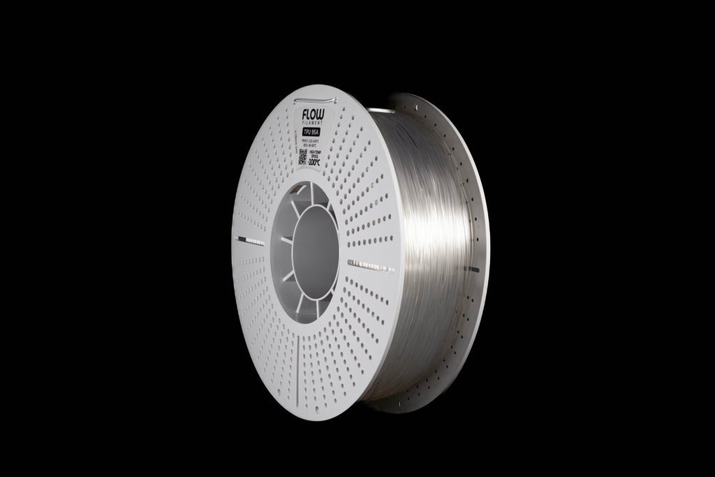 A spool of transparent-colored 3D printing filament on a solid black background. The spool is white with a circular perforated design, and the brand name 'FLOW' is printed on the top.