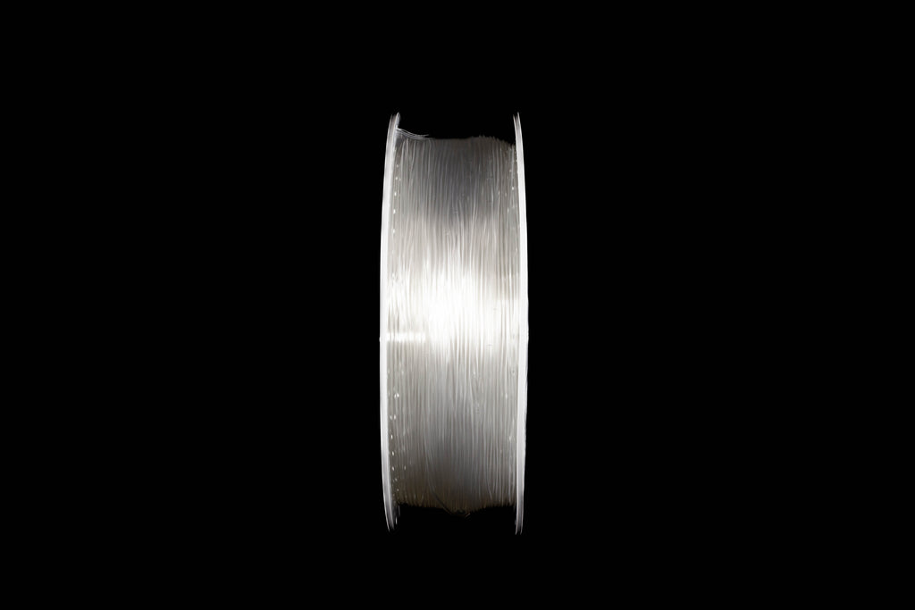A spool of transparent 3D printing filament wound tightly, shown vertically against a solid black background.