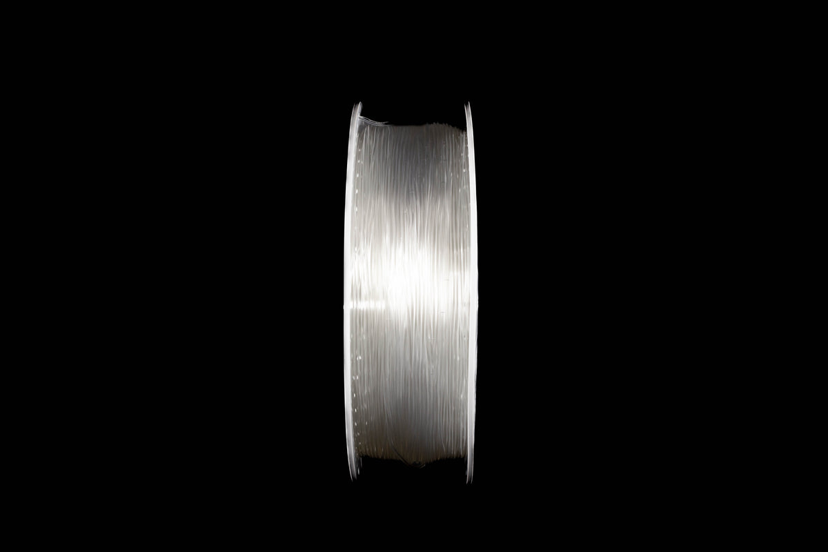 A spool of transparent 3D printing filament wound tightly, shown vertically against a solid black background.