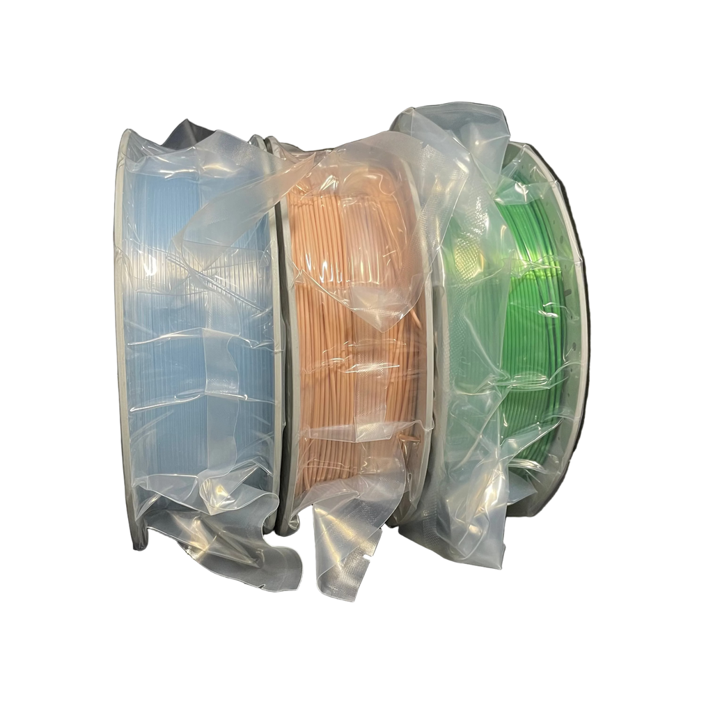 Three spools of 3D printer filament wrapped in clear plastic, showing light blue, peach, and green colors.
