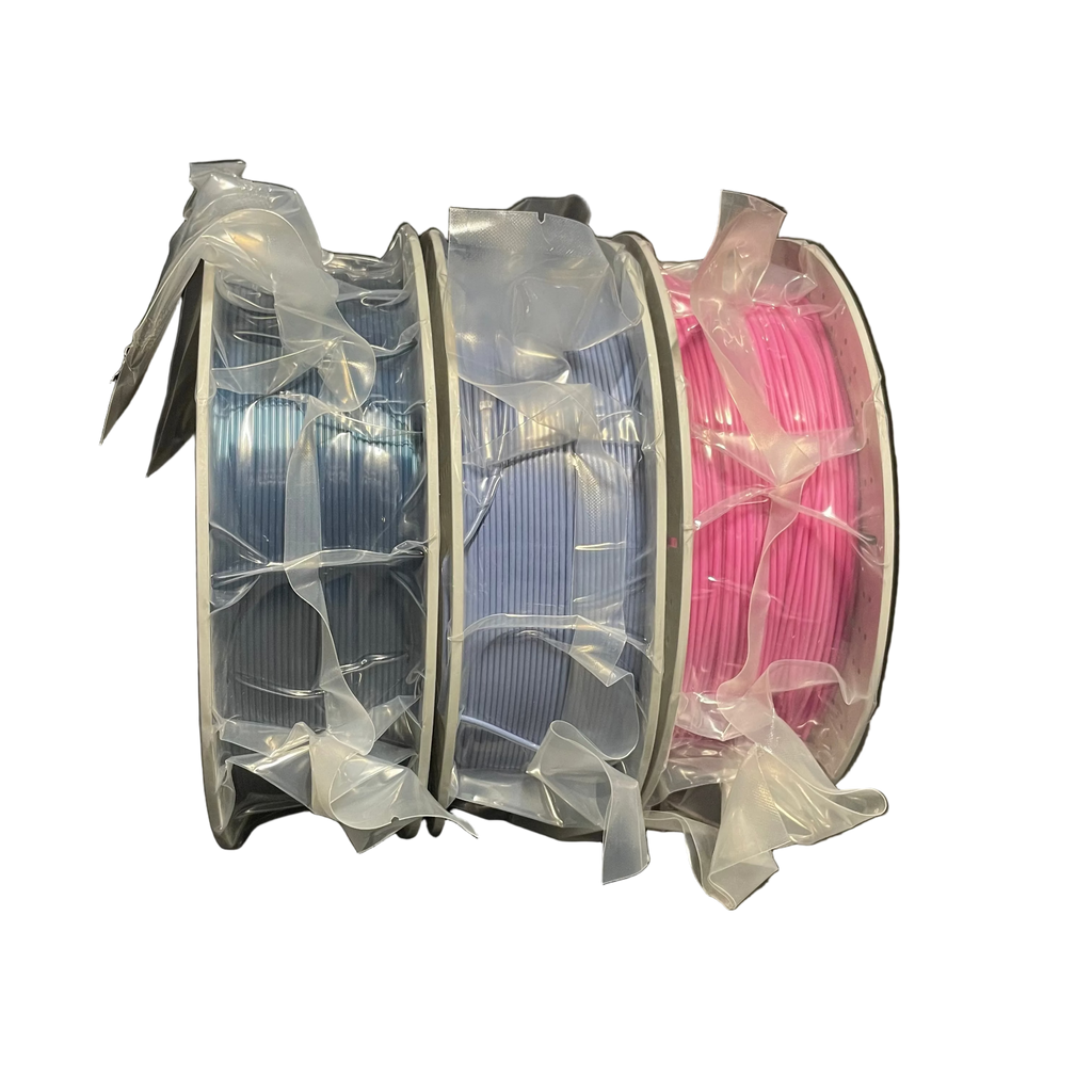 Three spools of 3D printer filament wrapped in clear plastic, showing light blue, lavender, and hot pink colors.